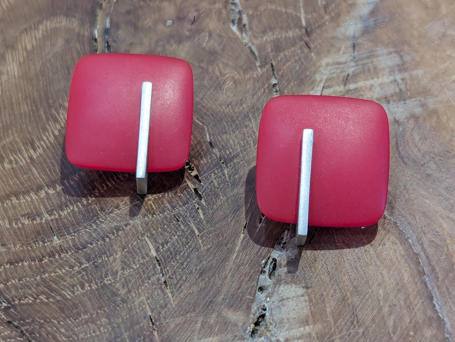 Red square earrings on a brown wooden background 