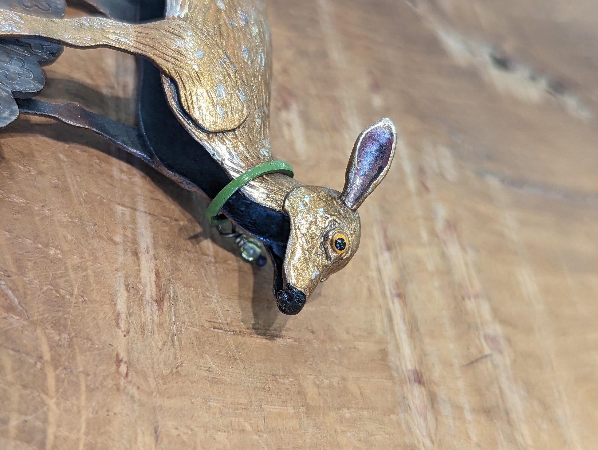 Close up of fawn coloured enamelled silver deer. The deer has a green collar and yellow eyes. The deer has silver markings on it's skin