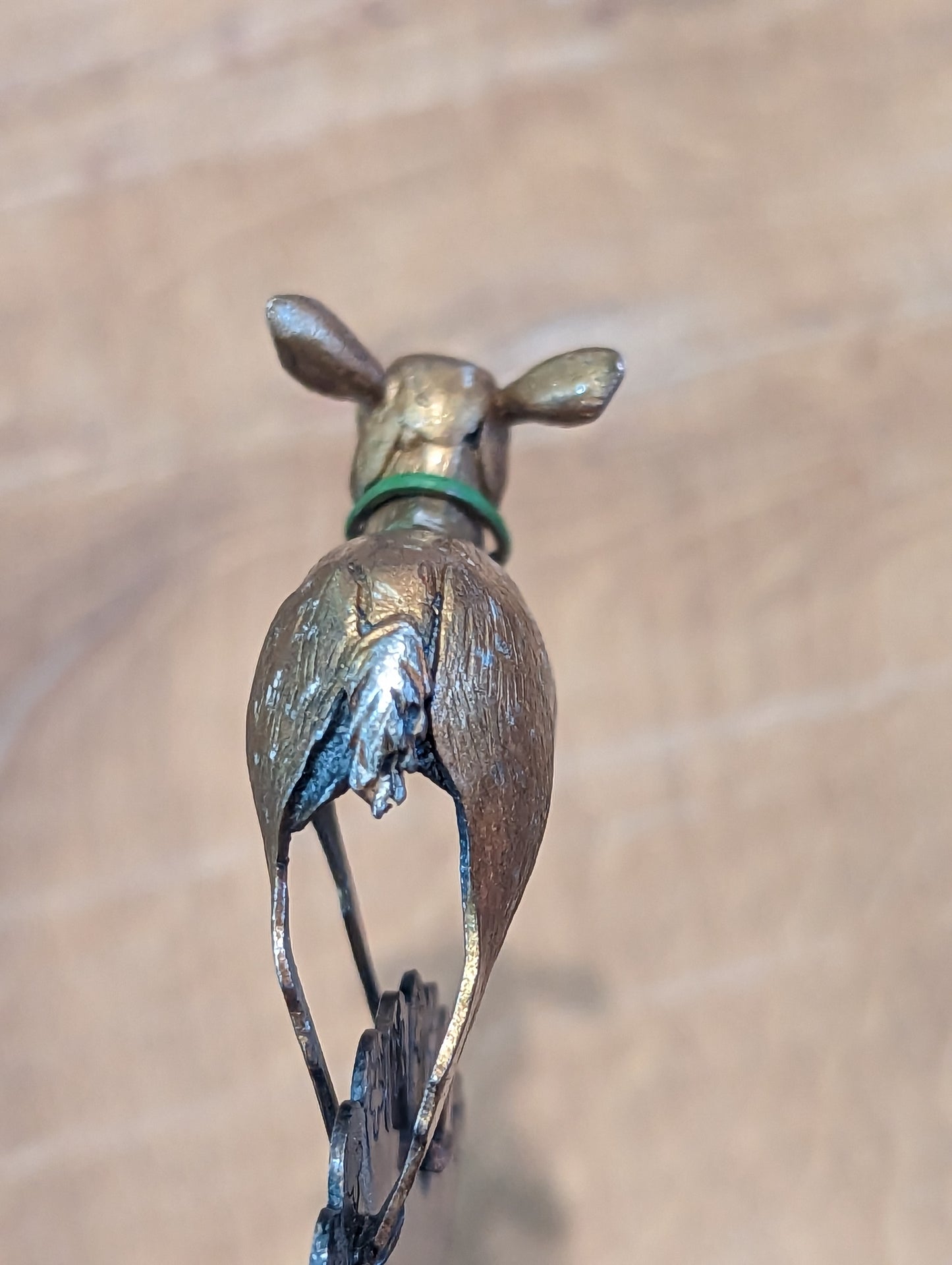 Rear view of the deer. It has a silver tail, green collar and it's ear's stand proud of it's head. It is golden with silver markings. 