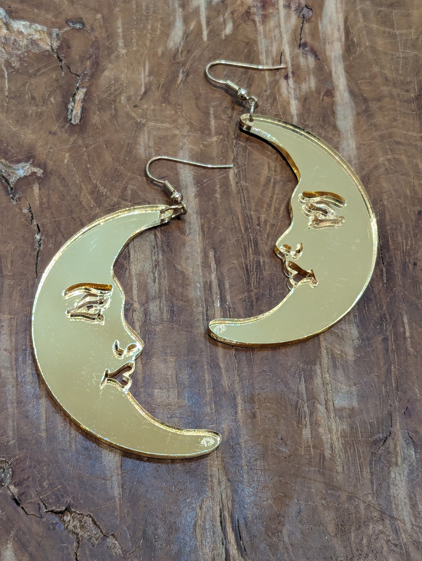 A pair of mirrored gold acrylic earrings in the shape of crescent moons with female faces. 