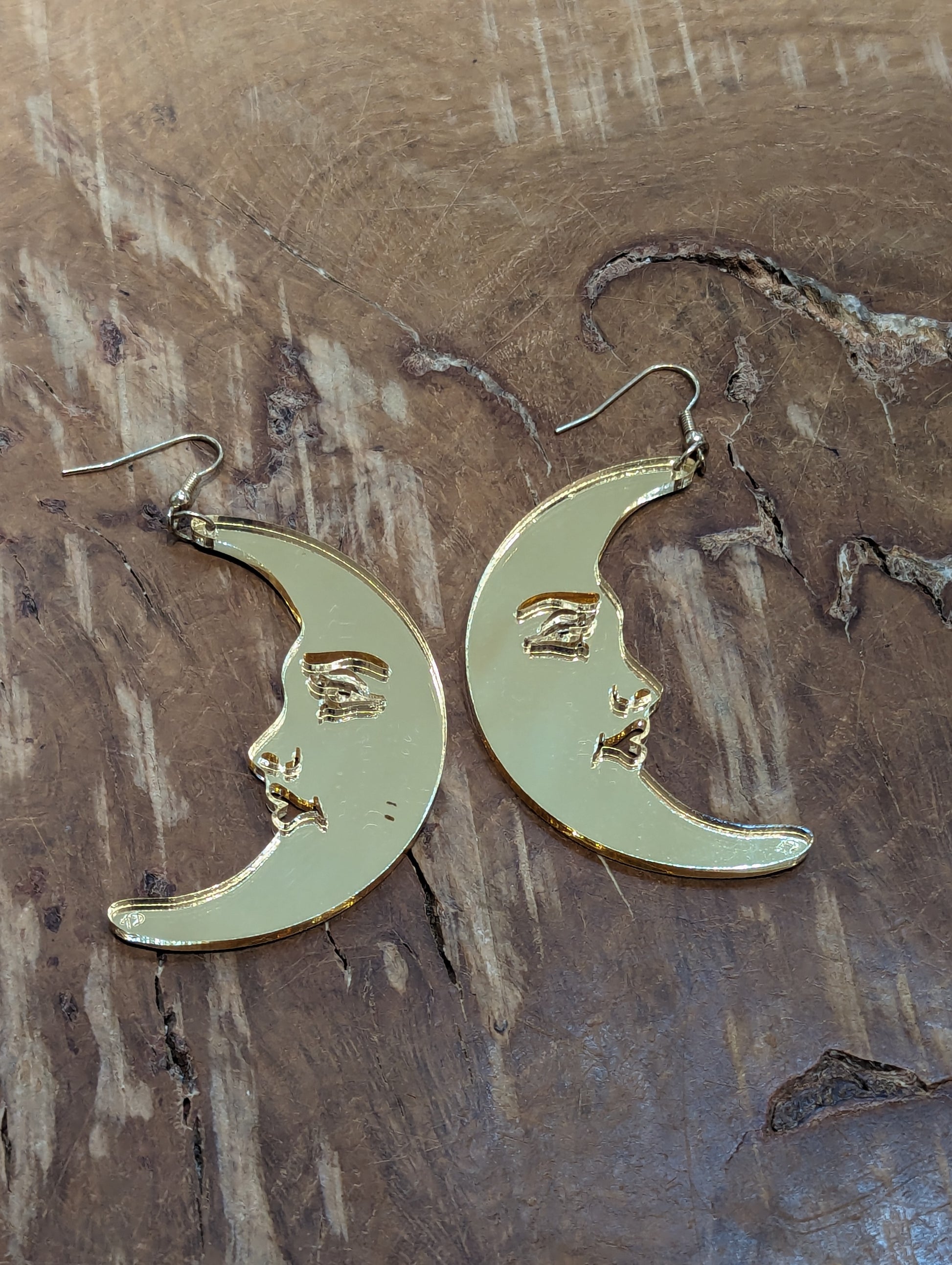 A pair of mirrored gold acrylic earrings in the shape of crescent moons with female faces.