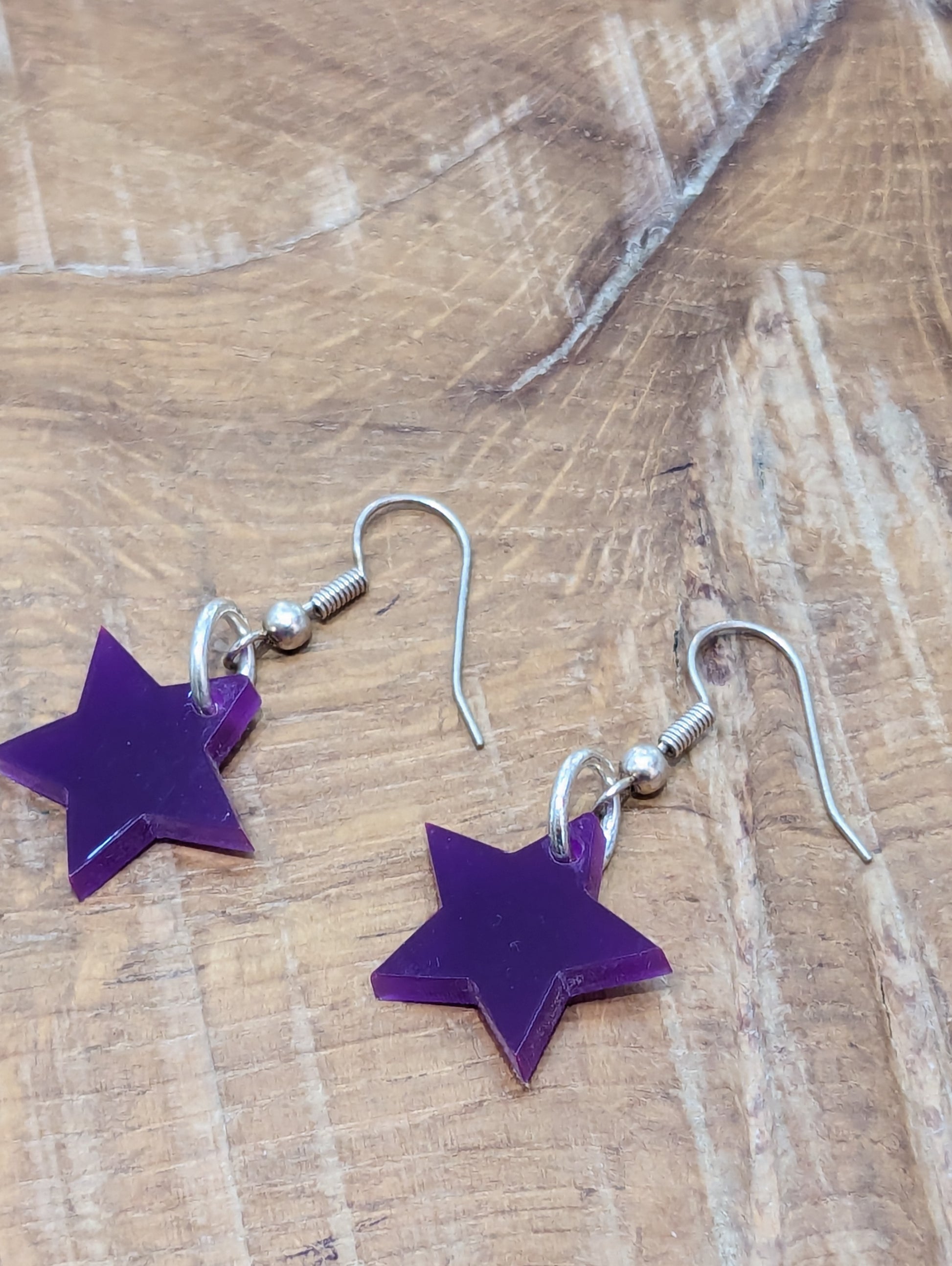 Bright Purple star earrings on silver hooks on a warm wooden background