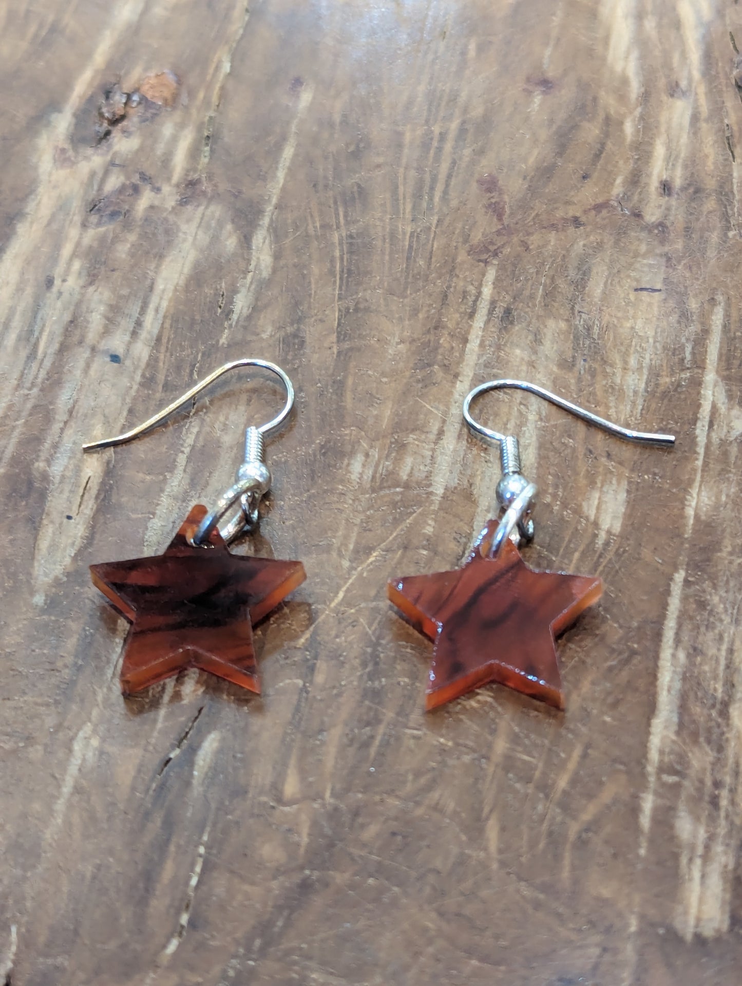 Two brown tortoiseshell star shaped earrings with silver earring hooks on a warm brown background. 