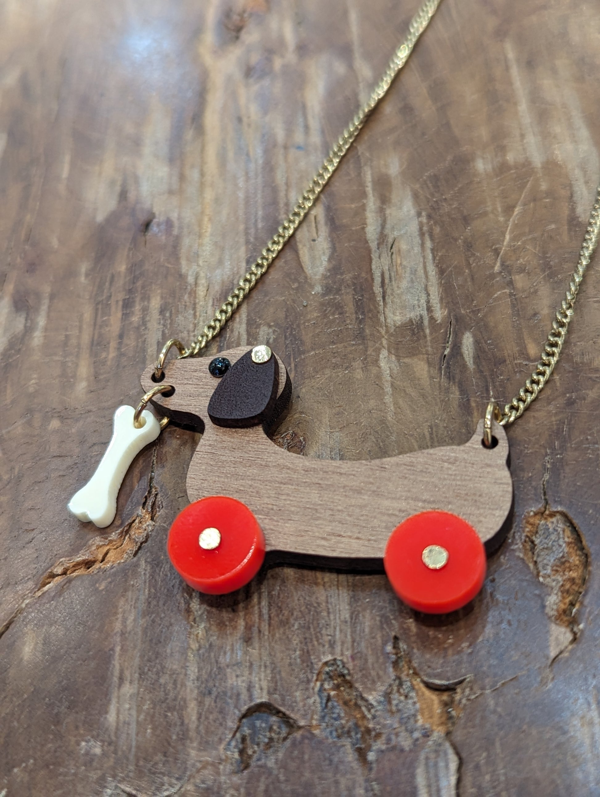  Brown wooden sausage dog with bright red wheels. The dog has a white bone dangling from his mouth. 