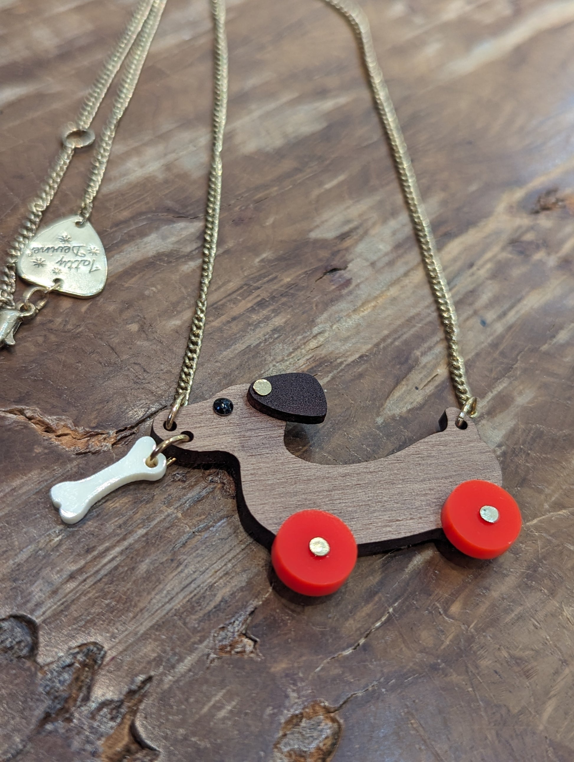 Brown wooden sausage dog with bright red wheels. Dog has a white bone dangling from their mouth. 